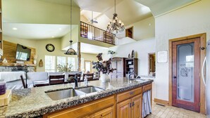 A spacious kitchen with granite countertops, wooden cabinets, and a large island. There is a dining area with a table and chairs, and a living room with a couch and a fireplace. - Grand Lake Waterfront Getaway w/ Boat Slip! (Eucha)