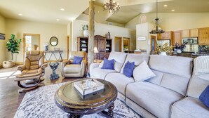 A spacious living room with a leather recliner, a beige sofa with blue pillows, a glass coffee table, and a chandelier. - Grand Lake Waterfront Getaway w/ Boat Slip! (Eucha)