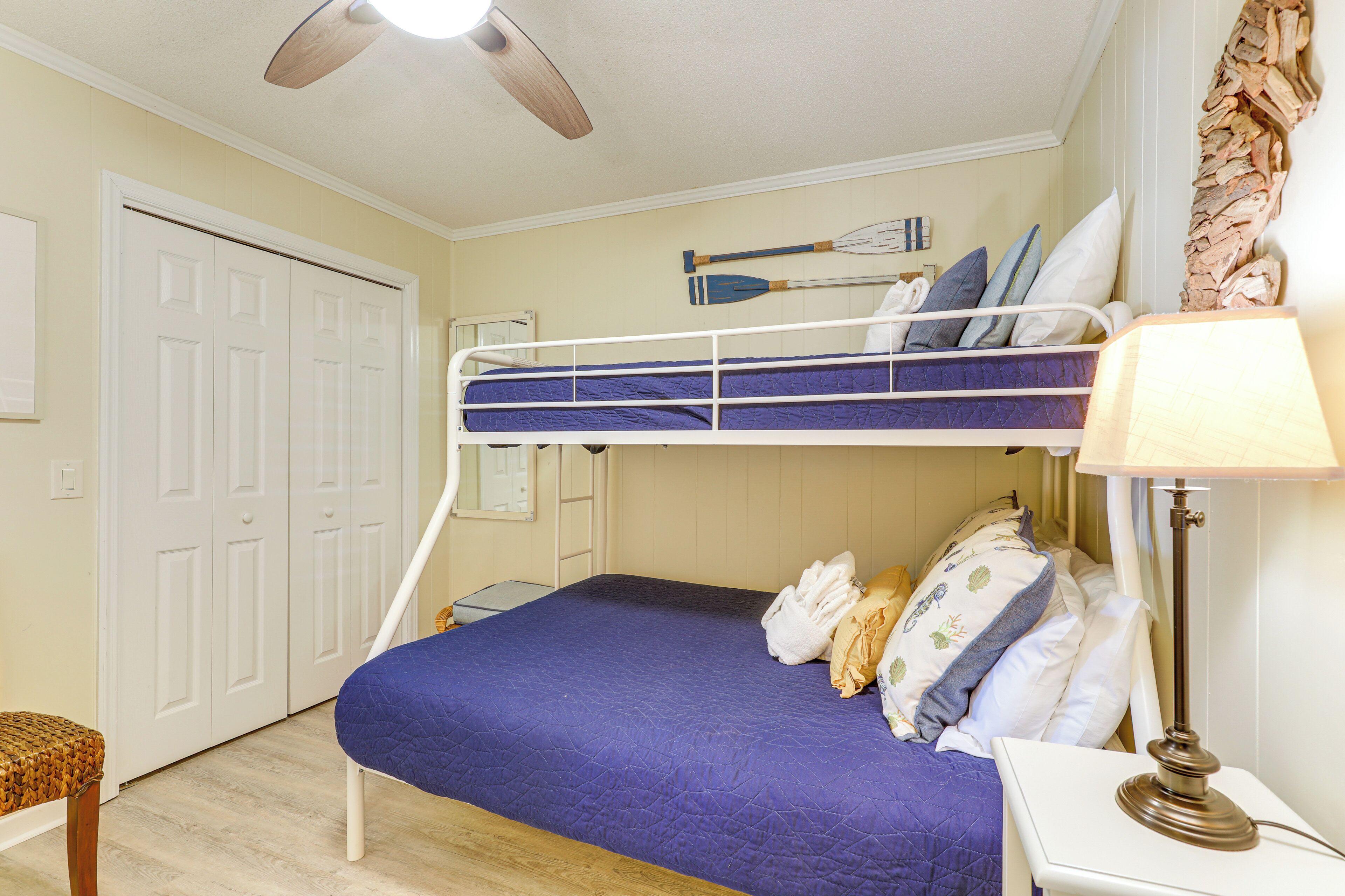 A bunk bed room with a ceiling fan, a bedside table with a lamp, and a door.