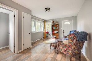 Ein Zimmer mit Holzboden, einem blumigen Sessel, einem Bücherregal und einer Tür zu einem weiteren Raum.