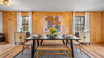 Un coin repas avec une table en bois dressée pour quatre personnes, entourée d’armoires en bois, d’un tapis à motifs et d’une tapisserie murale.