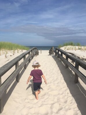 Ein Kind geht über einen sandigen Strand, vorbei an hölzernen Geländern, die zum Meer führen.