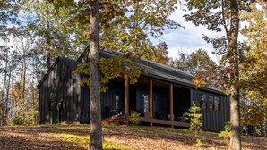 Un chalet rustique doté d’un porche, entouré d’arbres et d’un sol recouvert de feuilles.