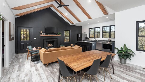 Une cuisine moderne dotée d’un îlot central, d’un coin repas avec une table et des chaises en bois, d’une cheminée noire et d’une grande fenêtre donnant sur un jardin.