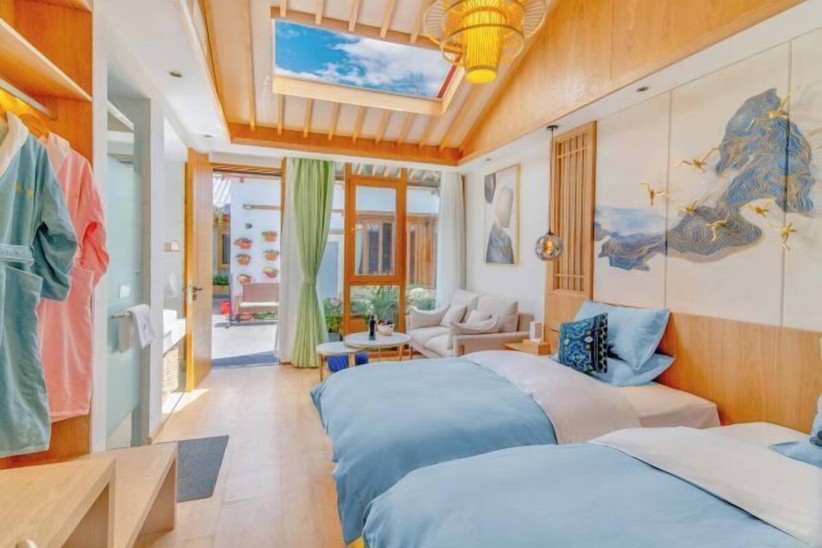 A hotel room with two beds, a wooden ceiling, a large window, and a wall mural.