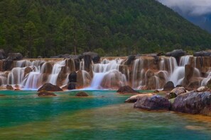 A waterfall with clear water and rocks in the foreground. - Anju·Rizhao Jinshan Designers' Panoramic Rooftop Cafe and Snow Mountain View (Lijiang)