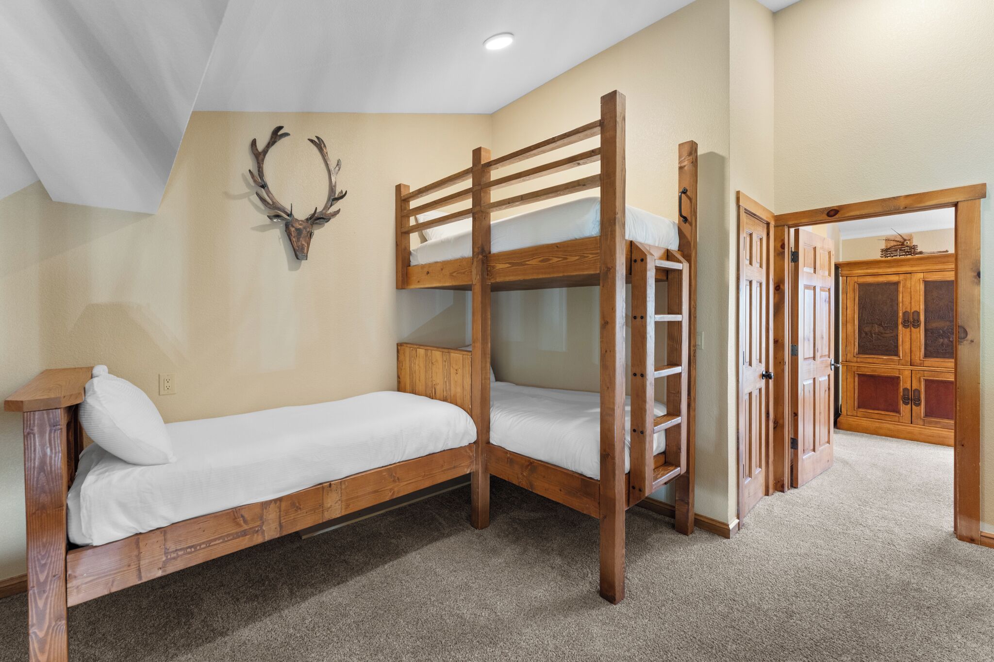A bunk bed room with a wooden headboard, a wall-mounted deer head, and a wooden cabinet.