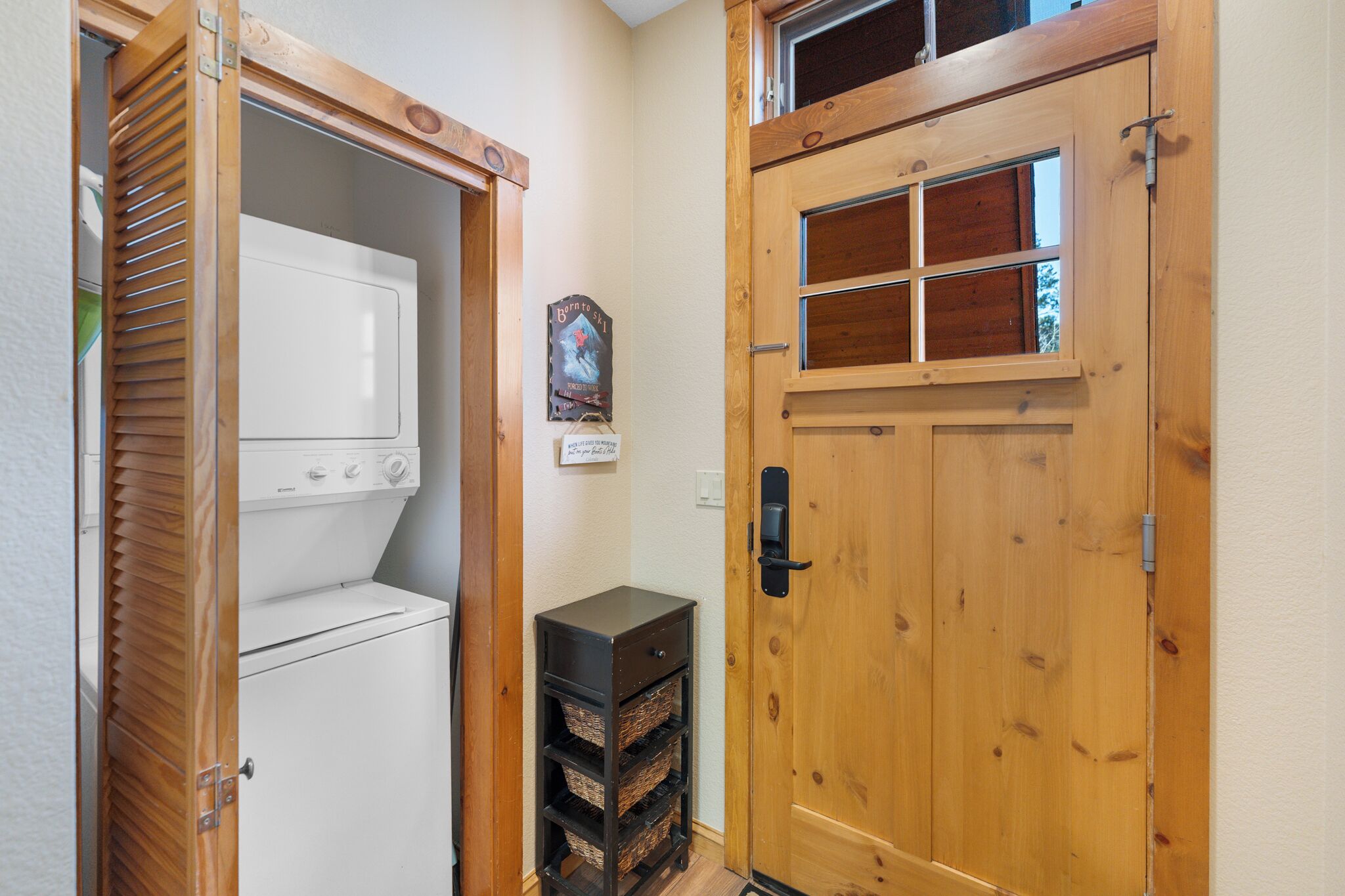 A laundry room with a white washer and dryer, wooden cabinets, and a door with a window.