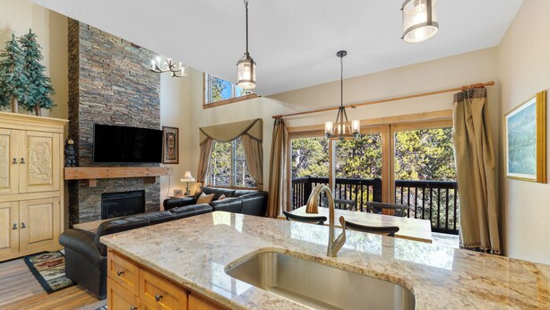 A spacious kitchen with a stone backsplash, a large island with a sink, and a fireplace. There is a black leather sofa and a dining area with a view of the outdoors. - Sk1841-2 (Keystone)