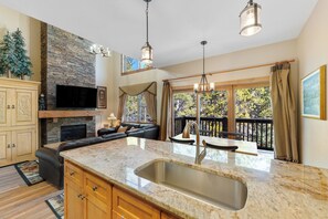 A spacious kitchen with a stone backsplash, a large island with a sink, and a fireplace. There is a black leather sofa and a dining area with a view of the outdoors. - Sk1841-2 (Keystone)