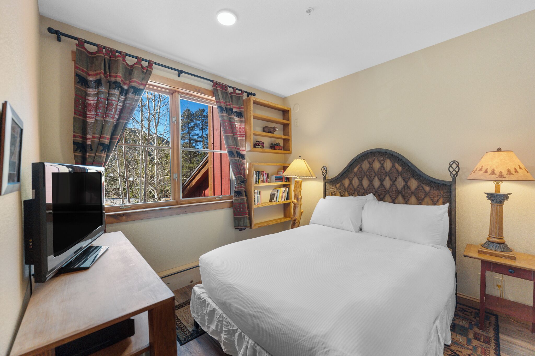 Een slaapkamer met een bed, een televisie, een boekenplank, een lamp en een raam met gordijnen.