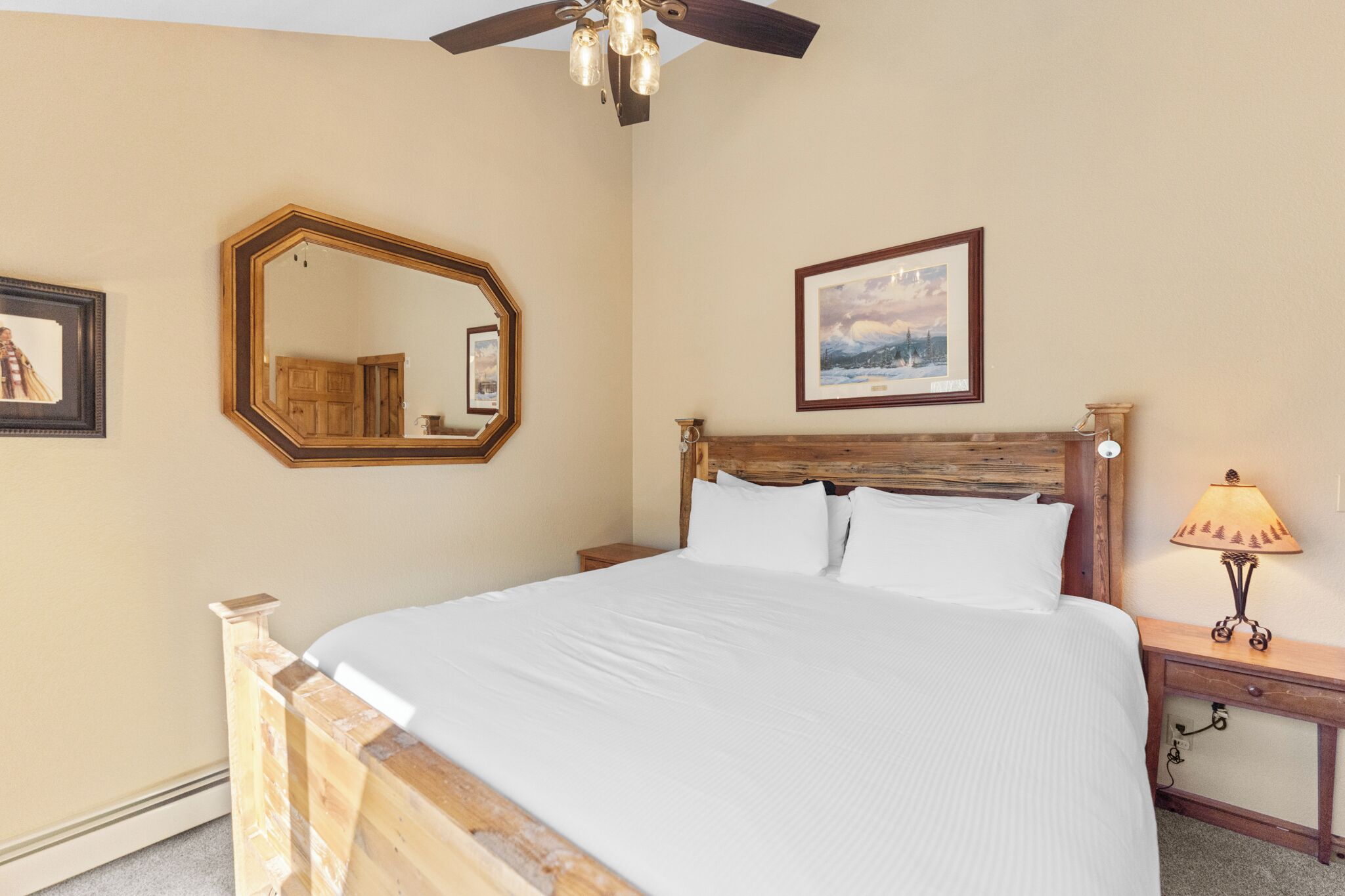 Une chambre à coucher avec une tête de lit en bois, un grand miroir, un tableau encadré, une lampe de chevet et une table de chevet en bois.