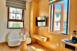 Una sala de estar moderna con un panel de pared de madera, un televisor de pantalla plana montado en la pared, un sofá blanco, una mesita redonda con un florero y un banco.