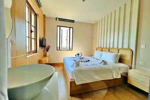 Habitación de hotel con una bañera grande, una cama con cabecero de madera y una ventana con persianas verticales.
