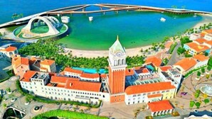 Vista aérea de un pueblo costero con un edificio blanco destacado con torre del reloj, un puente y una pequeña isla con parque acuático.