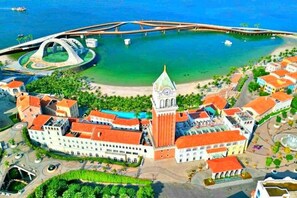 Vue aérienne d’une ville côtière, avec un beffroi imposant, un pont et un port de plaisance.