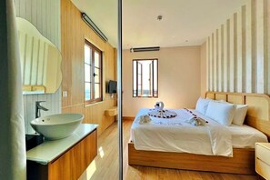 Un dormitorio moderno con una cama grande, cabecera de madera, un ventanal amplio y un baño con lavamanos sobre encimera.