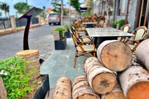 Un espace extérieur aménagé avec une table et des chaises, entouré de troncs d’arbres et de verdure.