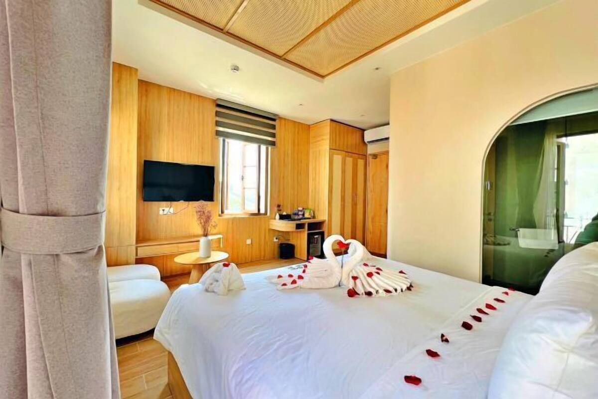 A hotel room with a large bed, wooden paneling, a flat-screen TV, a small table, and a shower area.