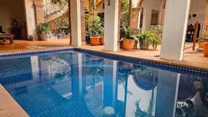 Piscina com bordas azuis em mosaico, rodeada por plantas em vasos e arcos.