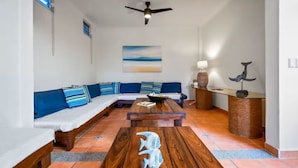 Uma sala de estar com uma mesa de centro de madeira, um sofá, um ventilador de teto e uma luminária na parede.