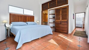 Um quarto com cama, mesa de cabeceira, guarda-roupa de madeira e janela.