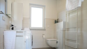 Un bagno moderno con lavandino, specchio e servizi igienici bianchi. Una finestra permette l'illuminazione naturale ed è presente un porta asciugamani con asciugamani.