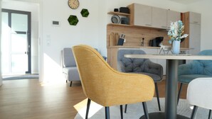 Un'area pranzo moderna con un tavolo rotondo, sedie gialle e grigie e una cucina sullo sfondo.