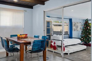 Un coin repas avec une table en bois et des chaises bleues, un canapé avec un matelas blanc et un sapin de Noël.