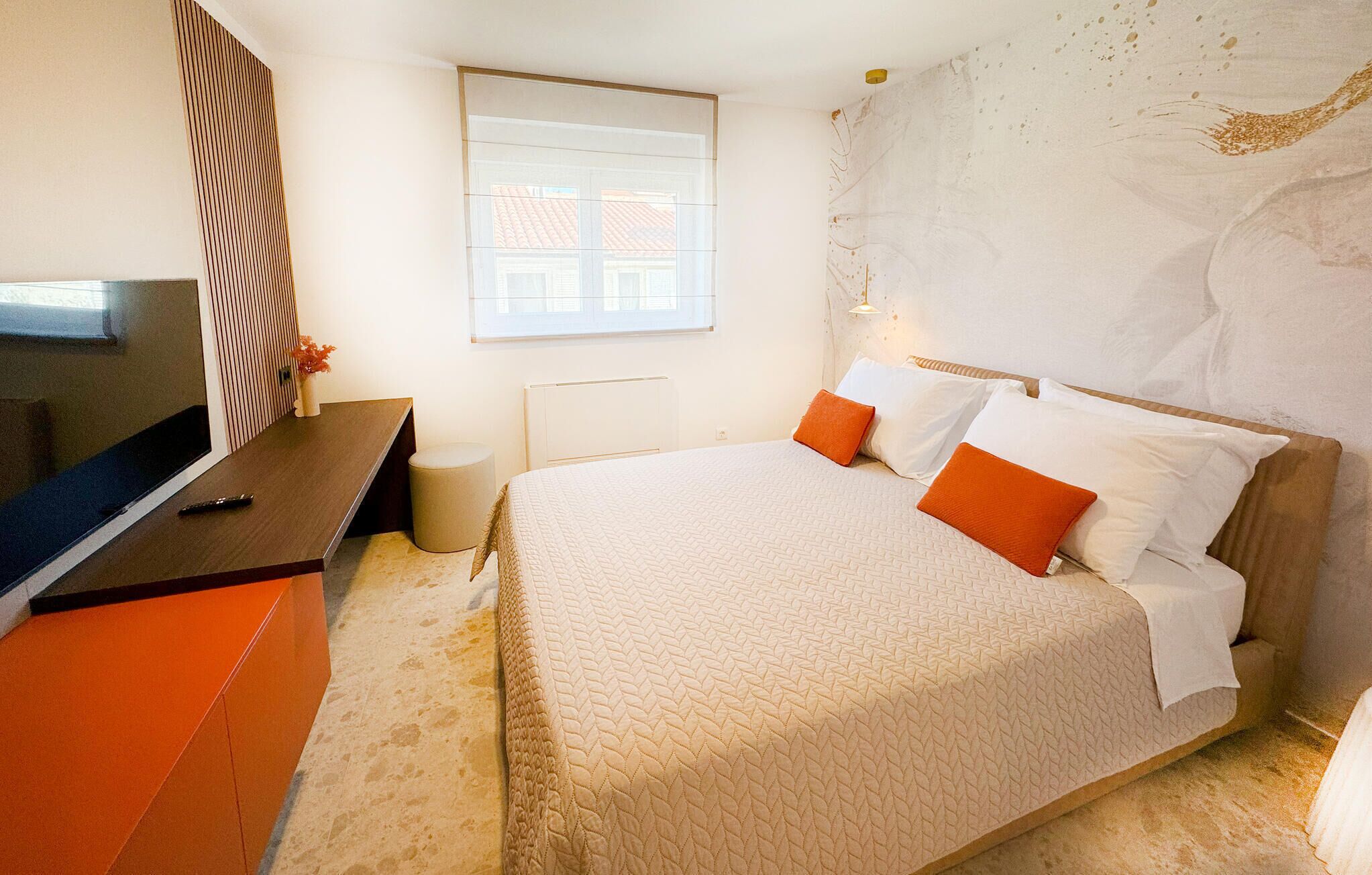 Quarto com uma cama, escrivaninha, cadeira, televisão e janela.