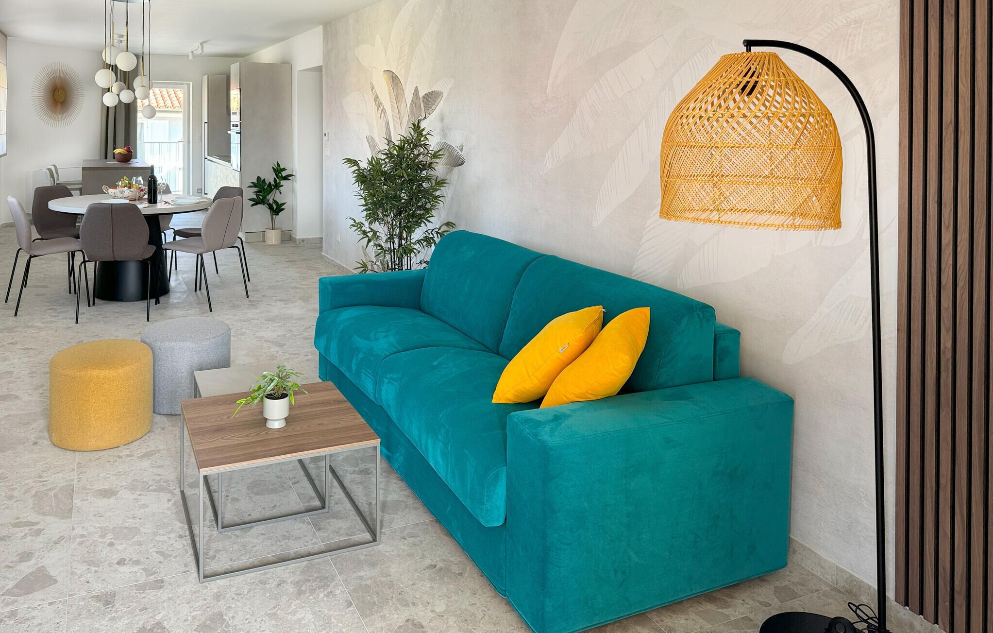 En tealgrøn sofa med gule puder, et træsofabord, en gul fodskammel og en hængende rattanlampe.