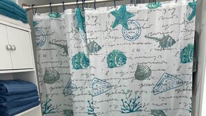 A bathroom with a white toilet, a blue towel on a shelf, and a shower curtain with a marine design. - Amazing Beach Location and Ocean View! Unit 220 (Daytona Beach)