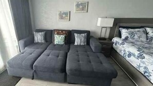 A room with a sofa bed, a bedside table, a lamp, and a bed with patterned bedding. - Amazing Beach Location and Ocean View! Unit 220 (Daytona Beach)
