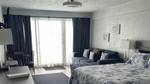A bedroom with a bed, a desk, a chair, and a window with curtains. - Amazing Beach Location and Ocean View! Unit 220 (Daytona Beach)
