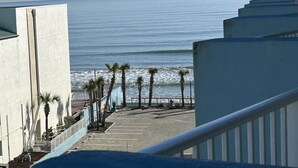 Vista da un balcone su una spiaggia con palme e cielo sereno.