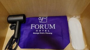 Un sac de l’hôtel, de couleur violette, sur lequel est imprimé le nom « FORUM HOTEL George Town, Penang », un sèche-cheveux noir et un objet blanc enveloppé dans du plastique.