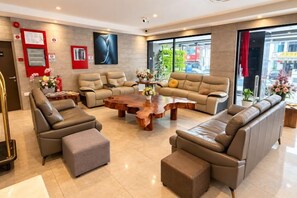 A modern living room with leather sofas, a wooden coffee table, and a large window offering a city view. - Forum Hotel Penang (George Town)
