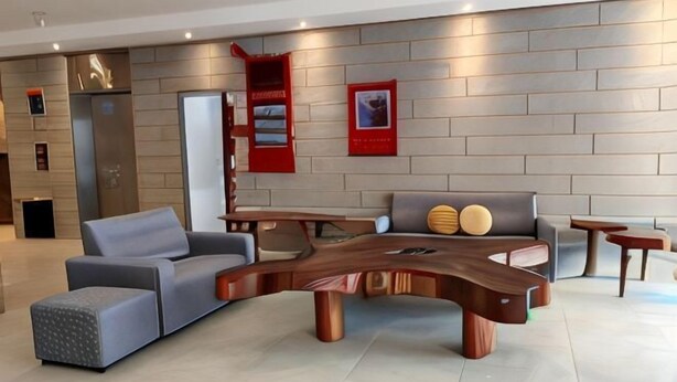 Un hall d’entrée moderne avec une table en bois aux lignes courbes, des canapés gris et un panneau rouge fixé au mur.