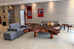 A modern living area with a curved wooden coffee table, grey sofas, and a red accent wall. - Forum Hotel Penang (George Town)