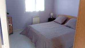 A bedroom with a bed, a nightstand, a radiator, a window, and a painting on the wall. - T2 48m² Soulac sur mer (Soulac-sur-Mer)
