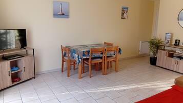 Un área de comedor con una mesa y sillas, un televisor sobre un mueble bajo y un armario con estante.