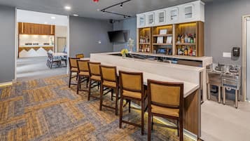 Uma área de bar com um balcão comprido, banquetas e uma televisão na parede.
