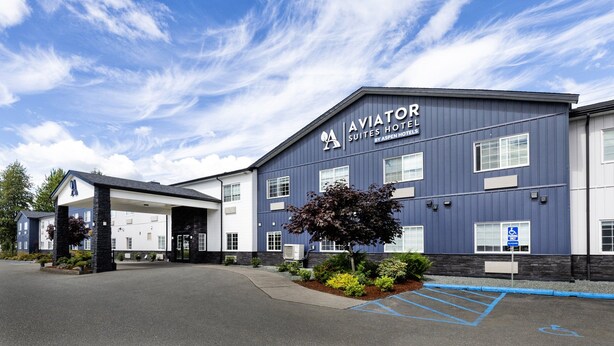 Un hôtel avec une enseigne indiquant « AVIATOR SUITES HOTEL BY ASPEN HOTELS » et un espace de stationnement accessible aux personnes handicapées.