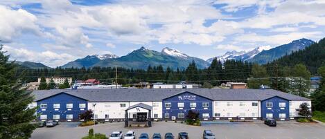 A hotel with a parking lot and a mountainous backdrop.