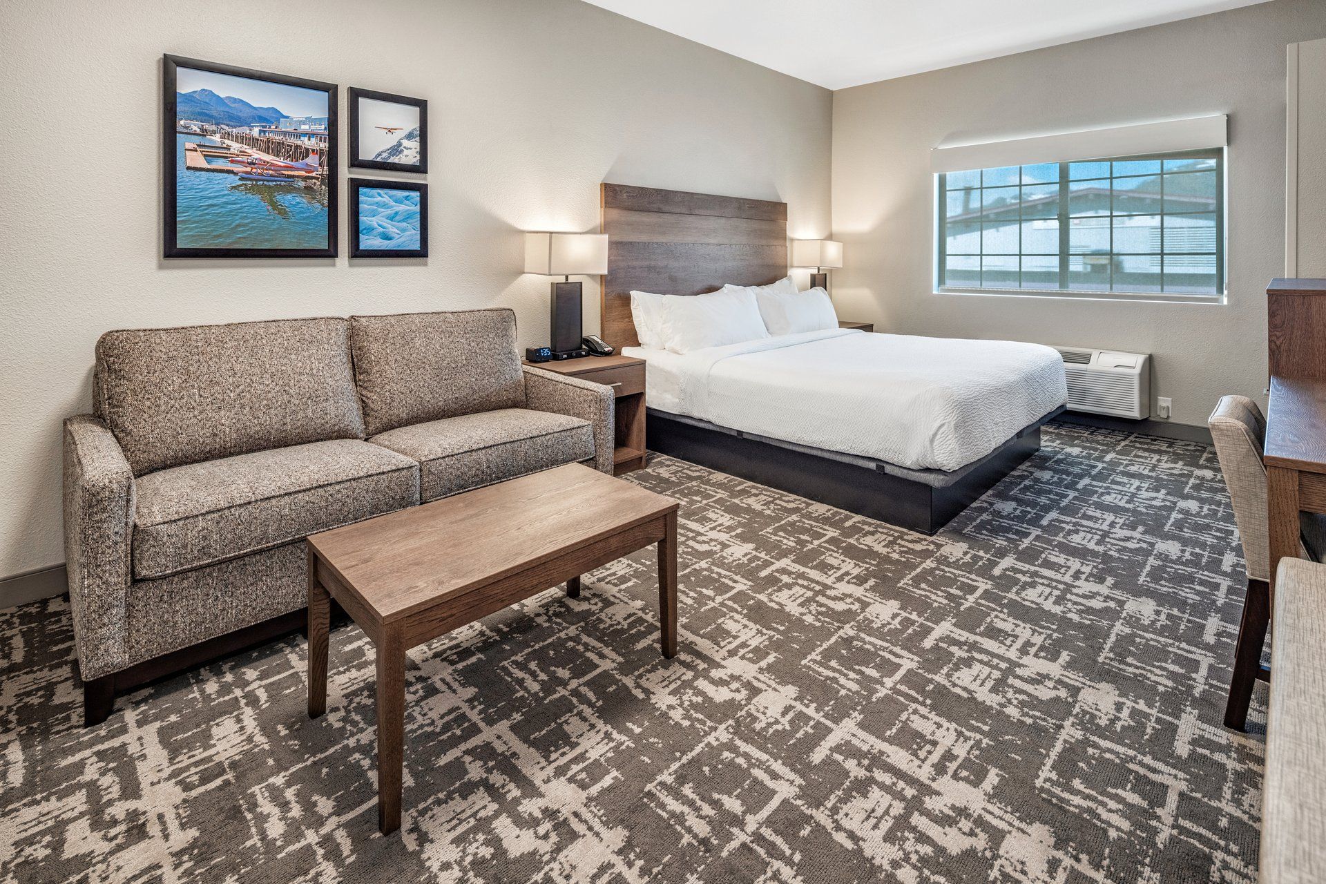 A hotel room with a bed, a sofa, a small table, and a window.