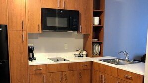 Een moderne keuken met houten kastjes, een zwarte magnetron, een spoelbak en een koffiezetapparaat.
