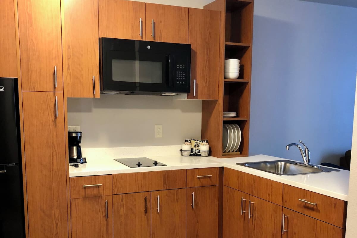A modern kitchen with wooden cabinets, a black microwave, a sink, and a coffee maker.