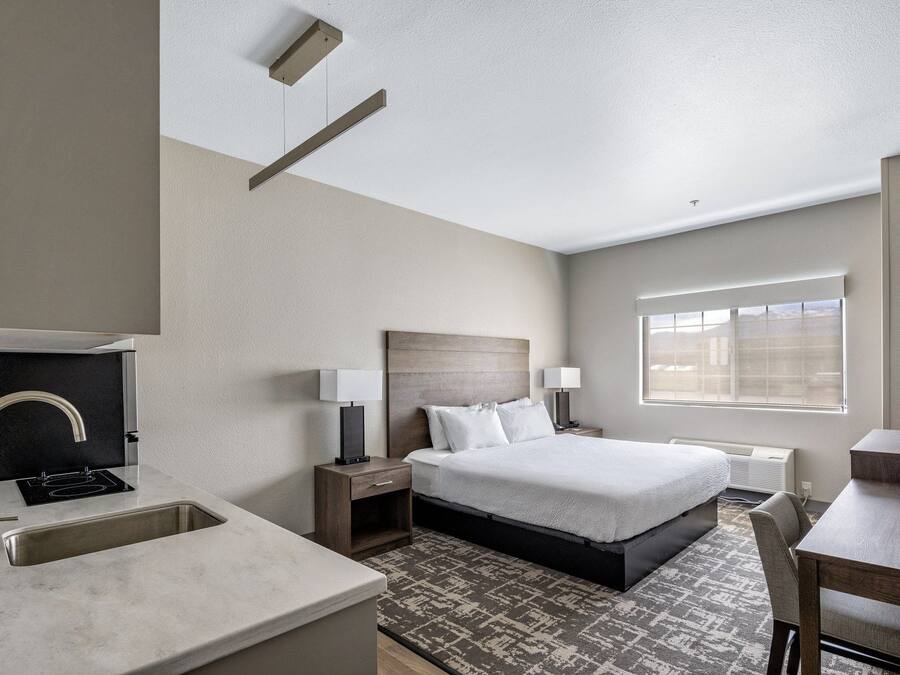 Habitación de hotel con cama, mesitas de noche, escritorio, ventana y baño con lavabo y espejo.