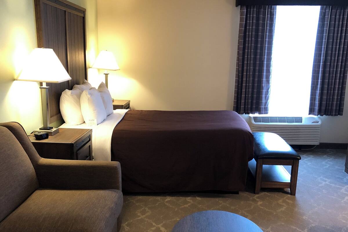 A hotel room with a bed, a sofa, a small table, and a nightstand with lamps.