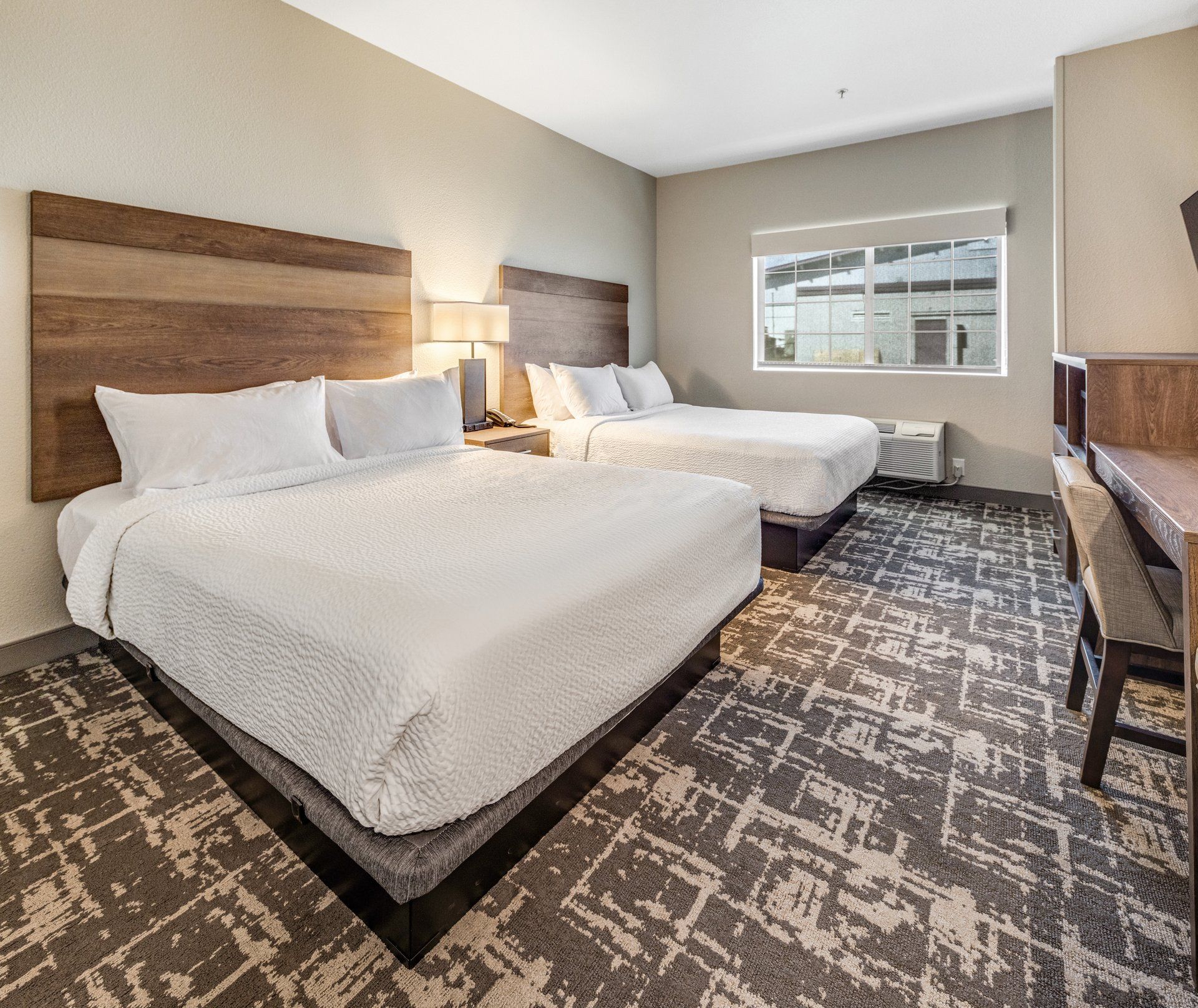 A hotel room with two beds, a large window, and a patterned carpet.